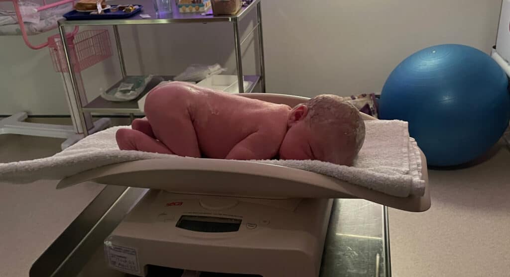 newborn baby on scales being weighed in delivery room